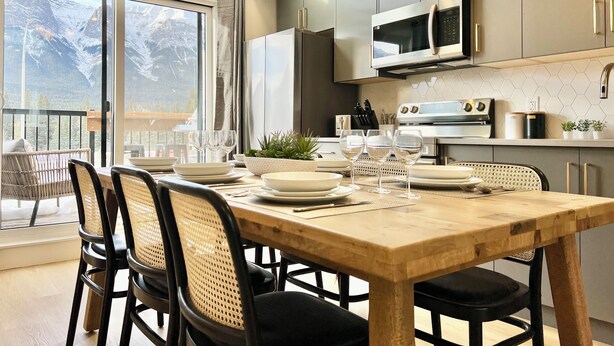 A modern kitchen with a large window, dining table set for four, and a view of mountains. - Separate-Address Combo • Hot Tub • Parking • Air Conditioner, Sleeps up to 17 (Harvie Heights)