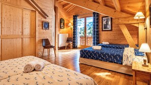 Une pièce de cabane en bois comprenant deux lits, une chaise, un bureau et une fenêtre avec des rideaux.