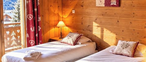 Quarto com duas camas, janela com vista para uma paisagem nevada, parede de madeira e um objeto decorativo na parede.
