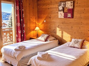 A room with two beds, a window with a view of a snowy landscape, a wooden wall, and a decorative piece on the wall. - 6 Bedroom Chalet - Stunning Sauna- Morzine-Avoriaz (Morzine)