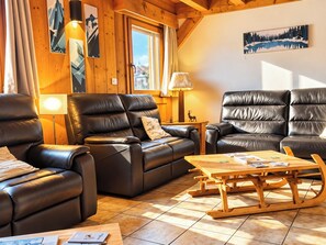A cozy living room with leather sofas, a wooden coffee table, and mountain-themed artwork on the walls. - 6 Bedroom Chalet - Stunning Sauna- Morzine-Avoriaz (Morzine)