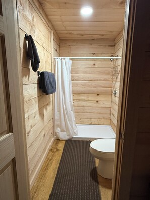 A wooden-paneled bathroom with a shower, a toilet, and a towel rack. - Fabulous cabin in Cordova perfect for your getaway!!! (Cordova)