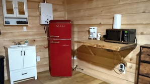 Cozinha compacta com geladeira vermelha, armário branco, cafeteira e micro-ondas em uma prateleira de madeira.
