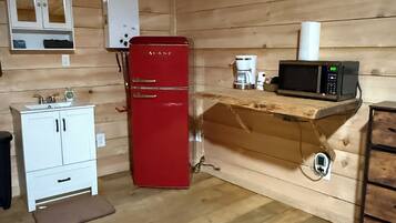 Eine kleine Küche mit einem roten Kühlschrank, einem weißen Schrank, einer Kaffeemaschine und einer Mikrowelle auf einem Holzregal.