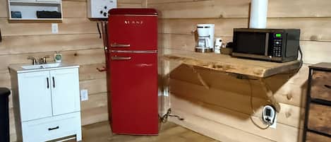 A compact kitchen with a red refrigerator, a white cabinet, a coffee maker, and a microwave on a wooden shelf.