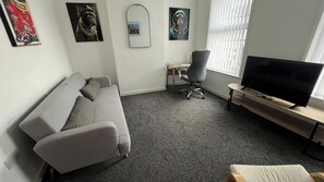 A living room with a grey sofa, a TV on a wooden stand, and a desk with a chair. - Apartment Sleeps 4 near Anfield (Liverpool)