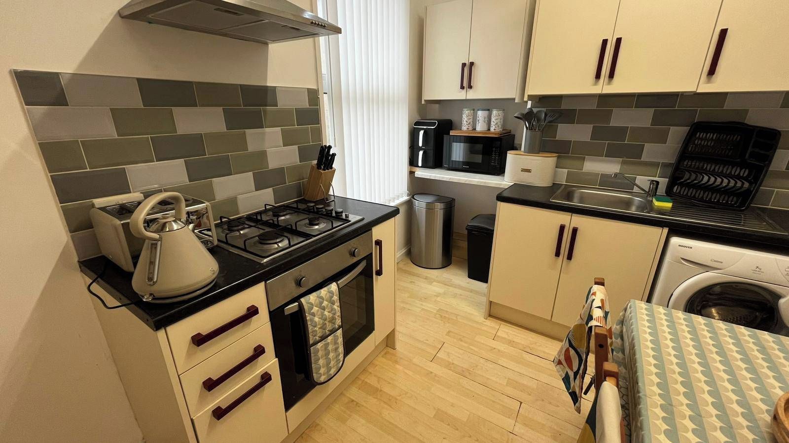 A compact kitchen with a gas stove, oven, and microwave. There is a sink with a dish rack, and a washing machine is visible in the background.