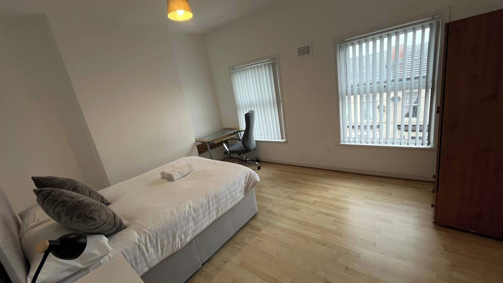 Un dormitorio con cama, escritorio, silla y dos ventanas.