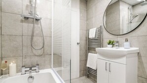 Ein modernes Badezimmer mit einer begehbaren Dusche, einem weißen Waschbecken mit Spiegel und einem weißen Schrank.