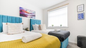 Ein Hotelzimmer mit zwei Betten, einem Fenster mit Jalousien, einer kleinen Pflanze und einem Bild an der Wand.
