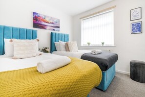 Ett hotellrum med två sängar, ett fönster med persienner, en liten växt och konstverk på väggen.