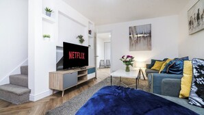 Ein modernes Wohnzimmer mit Fernseher, einer Couch, einem Couchtisch und einer Treppe.