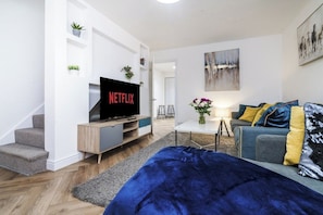 Ett modernt vardagsrum med en platt-TV, en soffa, ett soffbord och en trappa.