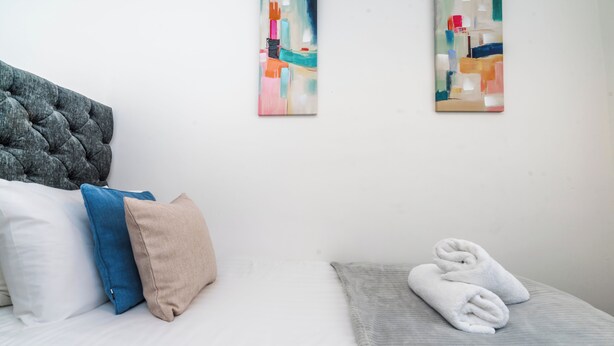 Ein Hotelzimmer mit einem Bett, Kissen, einem grauen Kopfteil und zwei abstrakten Bildern an der Wand.