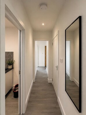 A hallway with a wooden floor, white walls, and a large mirror on the right. - 3 Bedroom House Sleeps 6 -Garden -Private Parking (Feltham)