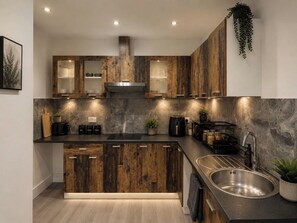 A modern kitchen with wooden cabinets, a stainless steel sink, and under-cabinet lighting. - House Sleeps 7 with WiFi (Feltham)
