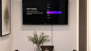 Moderni ruokailutila, jossa on seinälle asennettu taulutelevisio, puinen pöytä ja kuusi tuolia.