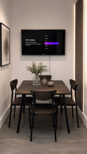 A modern dining area with a flat-screen TV mounted on the wall, a wooden table, and six chairs. - House Sleeps 7 with WiFi (Feltham)