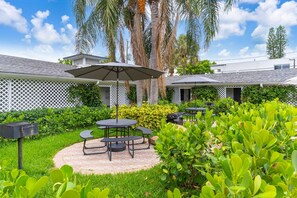 A patio area with a round table and chairs, surrounded by lush greenery and palm trees.
