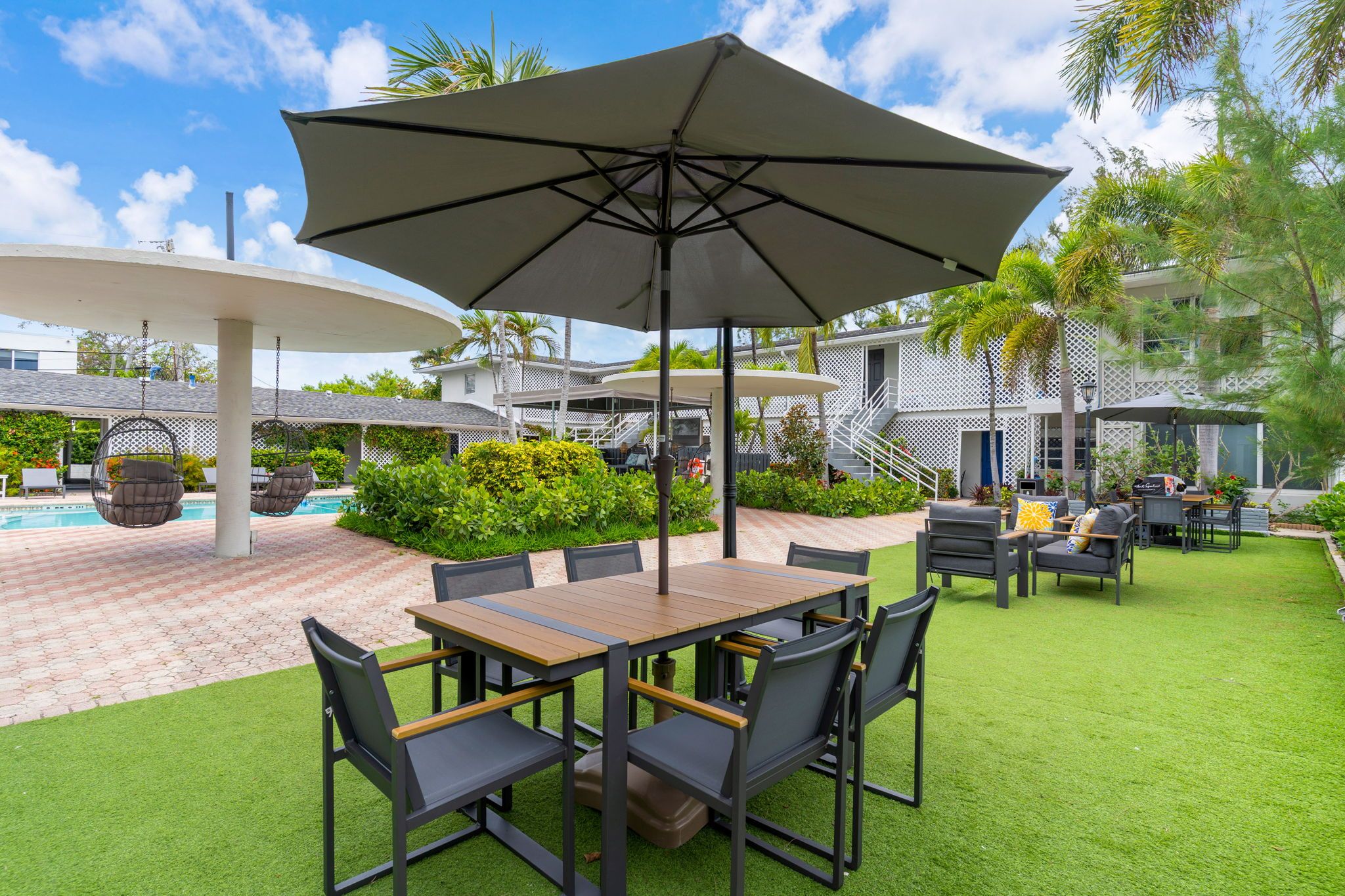 Un patio exterior con mesa y sillas, rodeado de vegetación y una piscina.