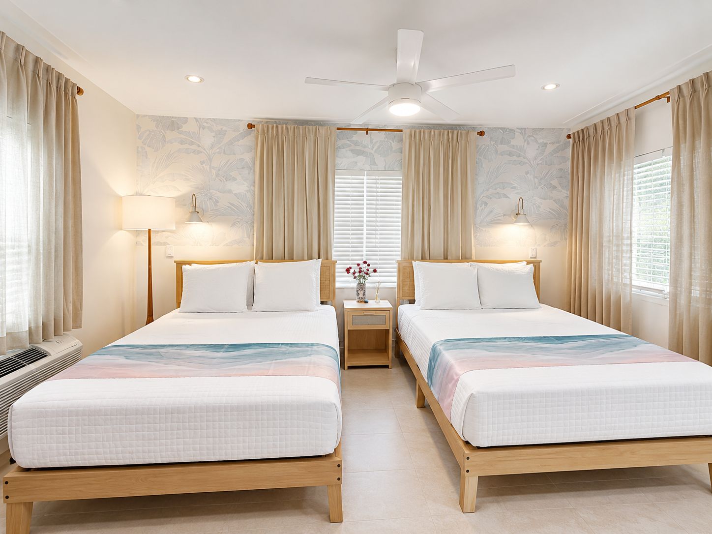 Habitación de hotel con dos camas, ventilador de techo, lámparas de noche y una ventana con cortinas.