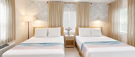 Habitación de hotel con dos camas, ventilador de techo, lámparas de noche y una ventana con cortinas.