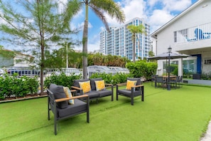 A hotel courtyard with outdoor seating, a pool, and a building with a blue logo. - Stylish Two‑Queen Bed Studio steps from the Ocean (Pompano Beach)