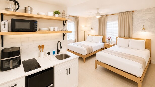 Une chambre d’hôtel avec une kitchenette, deux lits, un ventilateur de plafond et une fenêtre avec des rideaux.