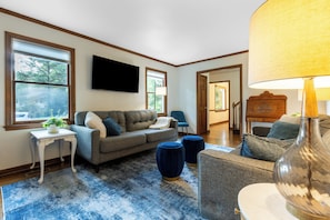 A living room with a grey sofa, a blue armchair, a white side table, and a floor lamp. - Whispering Pines- 5Br Wooded Retreat in Cary (Cary)