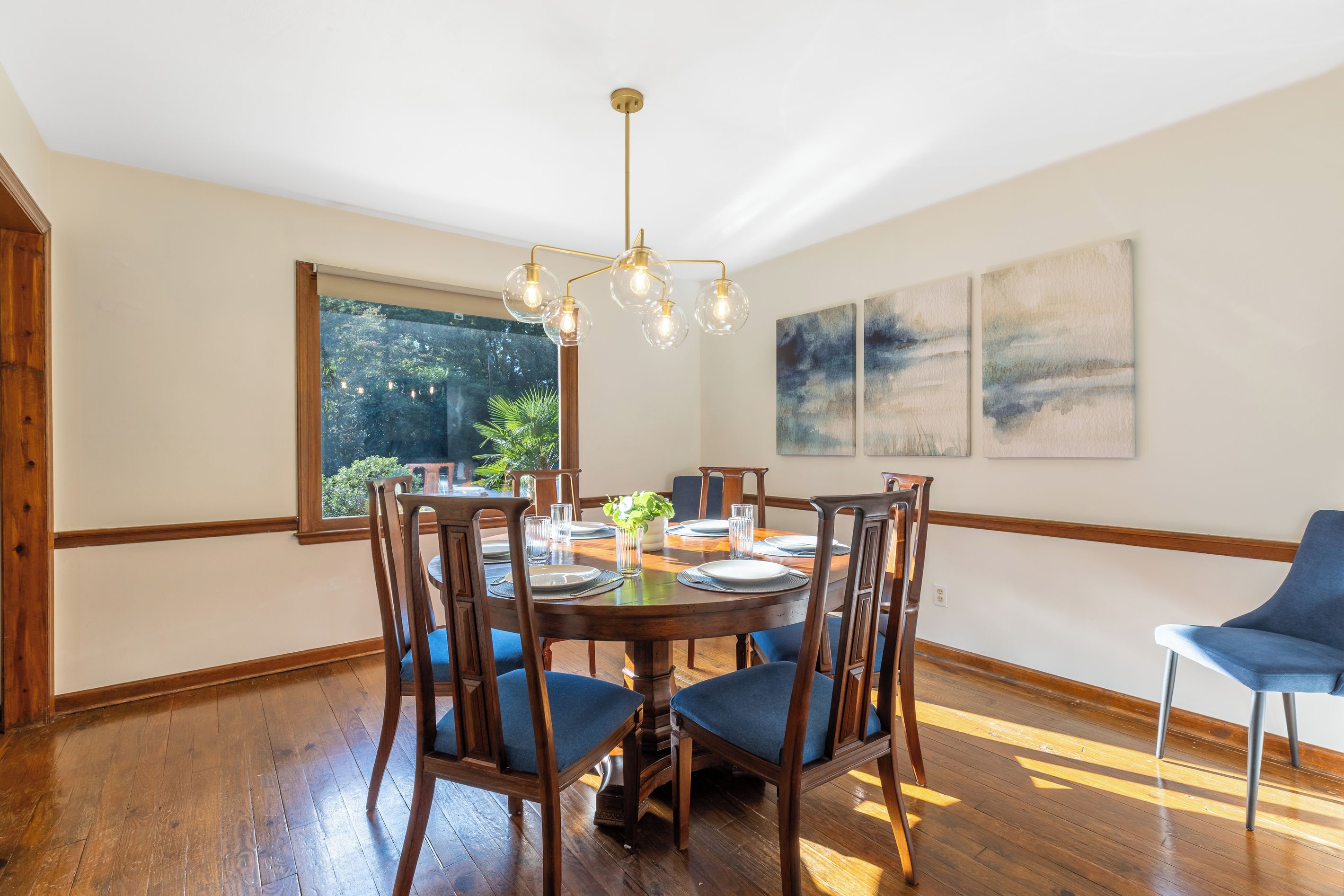 Een eetkamer met een ronde tafel, houten stoelen en een kroonluchter.