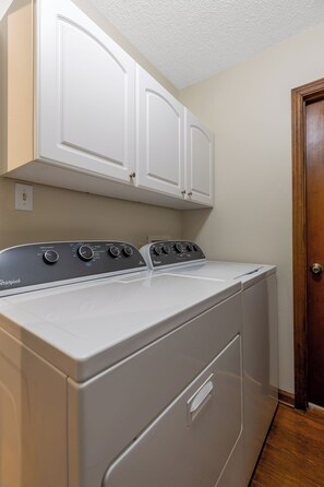 A Whirlpool washer and dryer in a laundry room with white cabinets above and a wooden door to the right. - Whispering Pines- 5Br Wooded Retreat in Cary (Cary)
