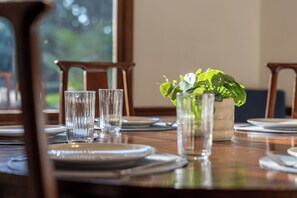 A dining table set with plates, glasses, and a vase with green foliage. - Whispering Pines- 5Br Wooded Retreat in Cary (Cary)