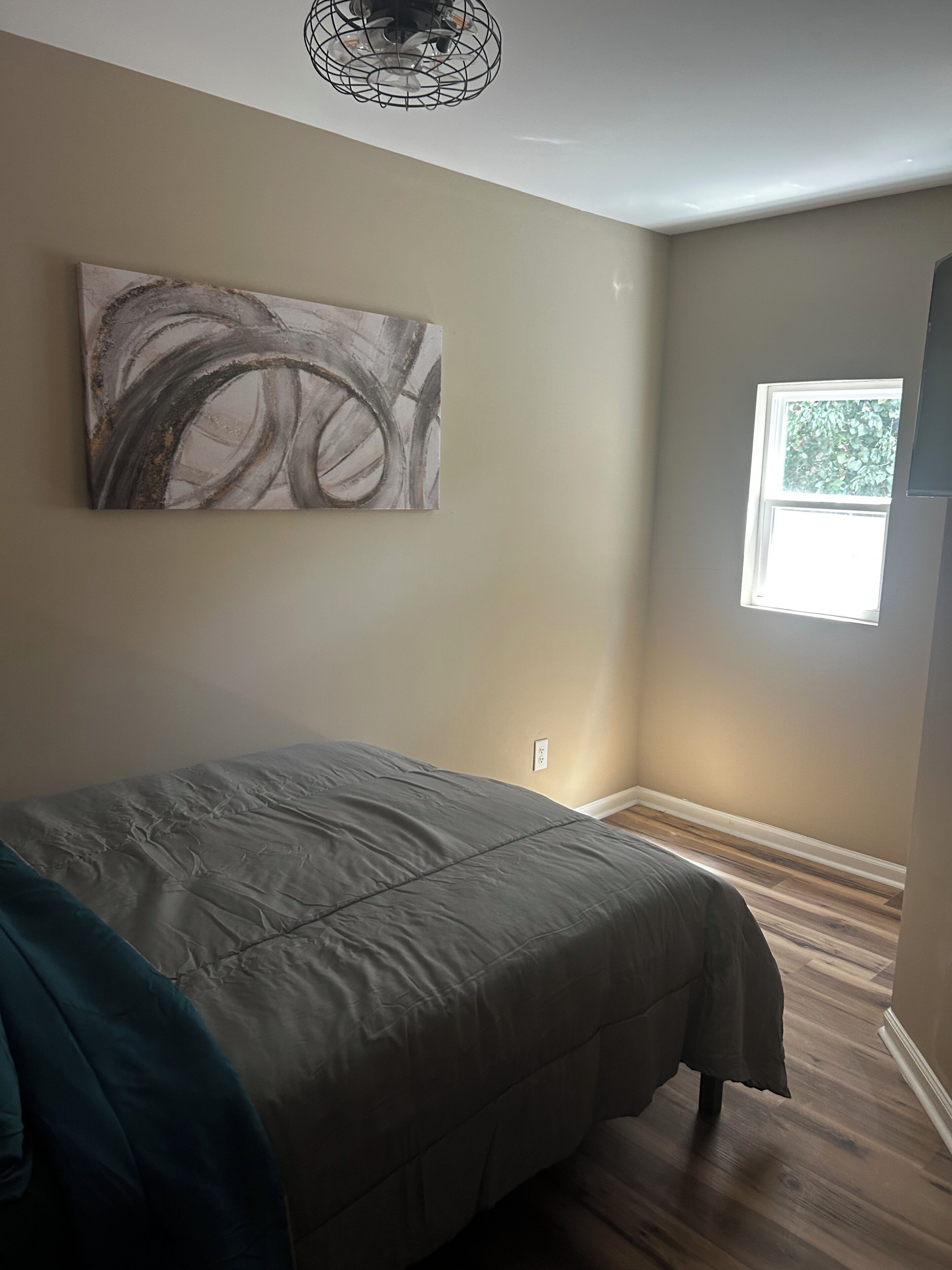 Un dormitorio con una cama, una ventana, una obra de arte en la pared y una lámpara en el techo.