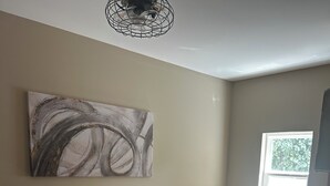 A bedroom with a bed, a window, a wall-mounted artwork, and a ceiling light fixture.