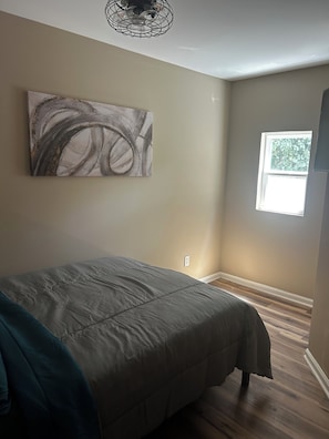 Une chambre à coucher avec un lit, une fenêtre, une œuvre d’art accrochée au mur et un luminaire au plafond.