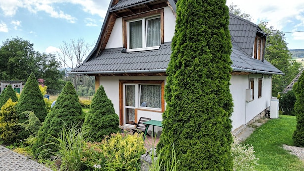 A two-story house with a sloped roof, a front porch with a bench, and a well-maintained garden with various shrubs and trees. - Gronik Mountain Resort 1 Apartment (Kościelisko)