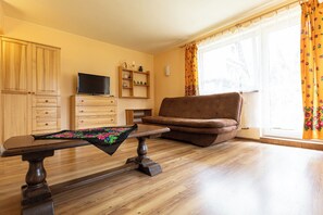 A living room with a wooden floor, a sofa, a television, and a table with a tablecloth. - Gronik Mountain Resort 1 Apartment (Kościelisko)