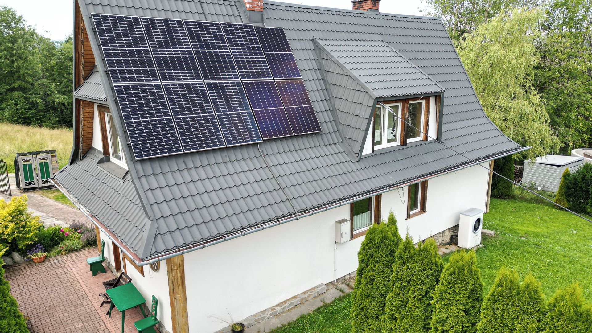 Ein Haus mit Satteldach, Solaranlagen, einem kleinen Garten und einem Schuppen.