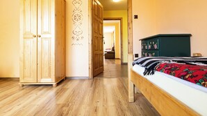 A room with a wooden wardrobe, a bed with a floral bedspread, and a hallway leading to another room. - Gronik Mountain Resort 1 Apartment (Kościelisko)