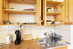 Eine Küche mit Holzausstattung, einem Wasserkocher, einer Kaffeemaschine, einer Spüle und verschiedenen Küchenutensilien.