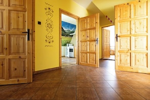 Un couloir avec des portes en bois et un sol carrelé, qui mène à une pièce dont un mur est décoré d’une fresque représentant un paysage de montagne.