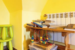 Une pièce avec un mur jaune, un bureau en bois sur lequel se trouvent des livres et un jouet, et un tabouret vert.