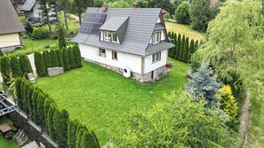 Ein zweistöckiges Haus mit geneigtem Dach, umgeben von einem gepflegten Rasen und Hecken.