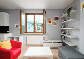 A modern living room with a red sofa, white coffee table, and a large window with a view of a bridge. There are shelves with books and decorative items, and a radiator below the window. - Park Praski Charming Apartment (Warszawa)