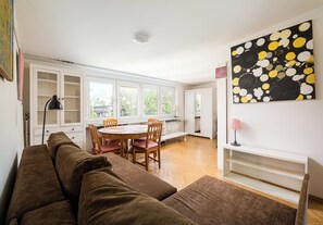 A living room with a brown sofa, a dining table with chairs, and a kitchen area with cabinets. - Ogród Saski Homely Apartment (Warszawa)