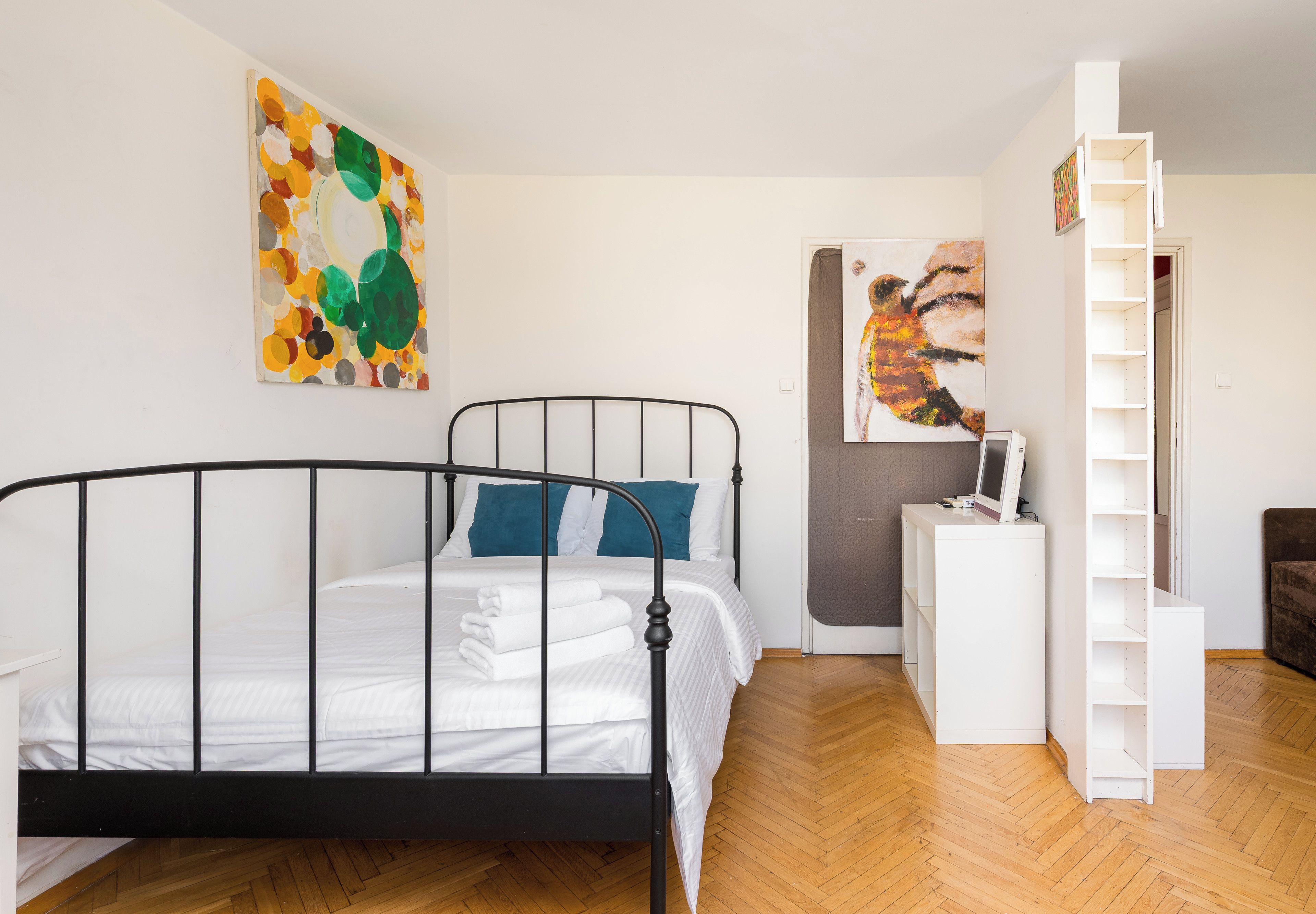 Ein Schlafzimmer mit einem Metallbettgestell, einem weißen Nachttisch, einer grauen Wand und einem Holzboden.