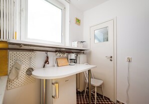 Una cocina con encimera blanca, cafetera, colgador de ollas y piso a cuadros.