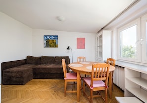 Una sala de estar con un sofá marrón, una mesa de comedor de madera con cuatro sillas y dos cuadros en la pared.
