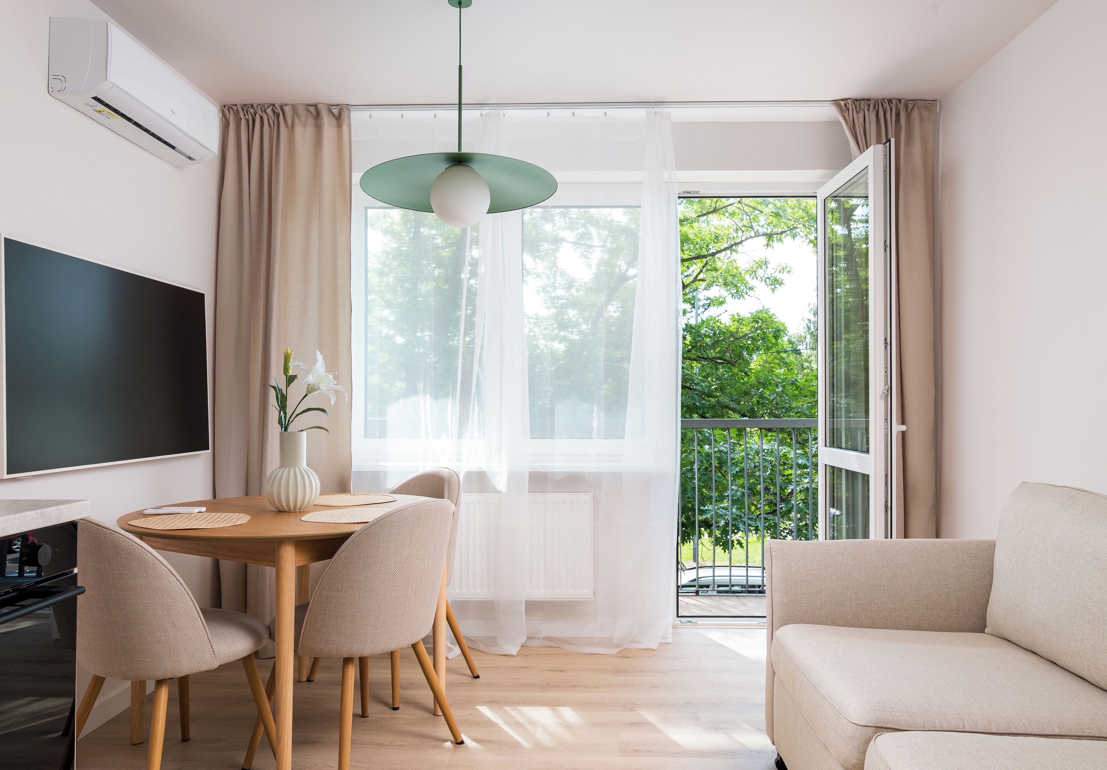 Ein modernes Wohnzimmer mit Essbereich, einem Flachbildfernseher, einer Couch und einem Balkon mit Blick auf Bäume.