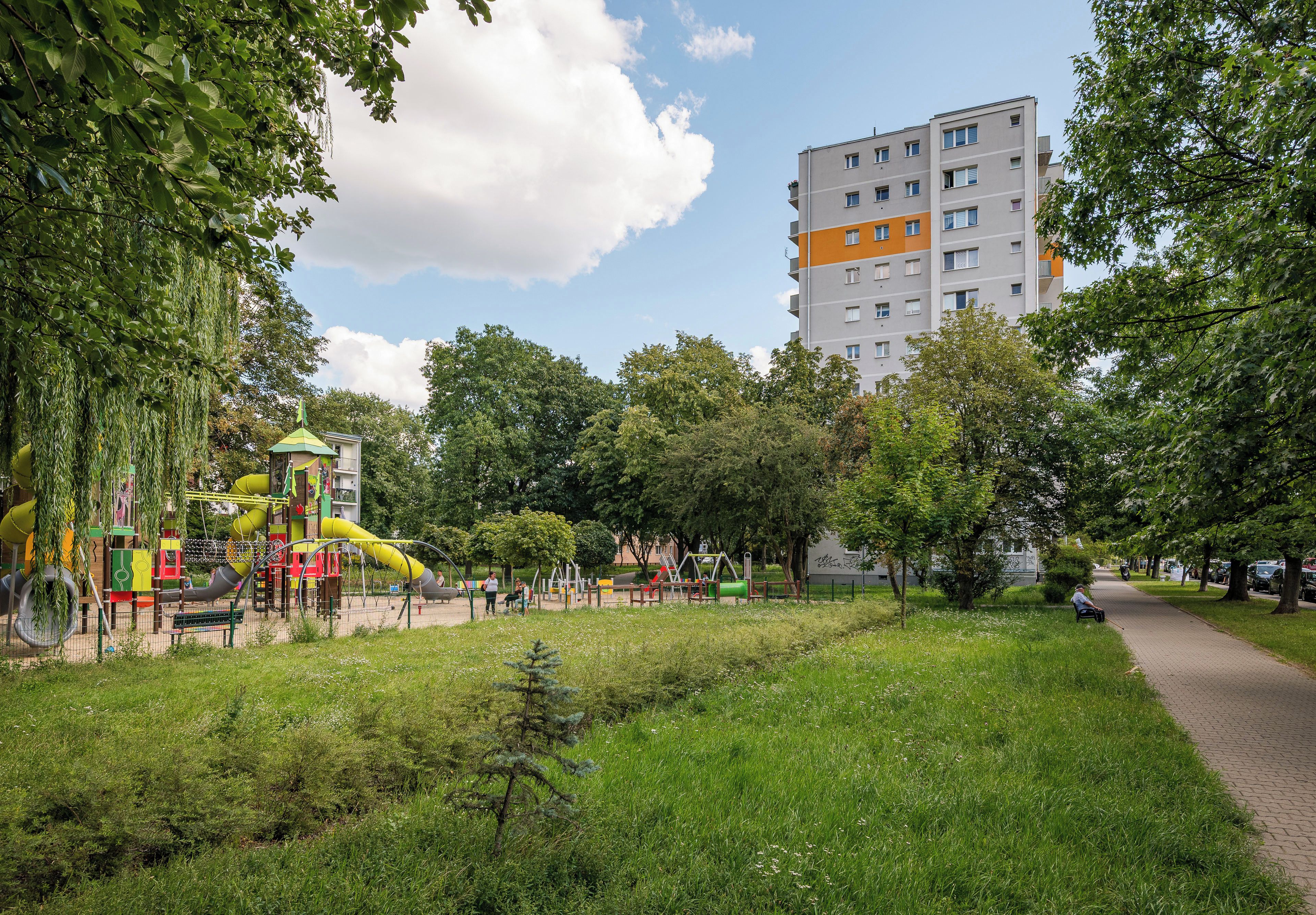 Ein Park mit Spielgeräten, einem Fußweg und einem mehrstöckigen Gebäude im Hintergrund.